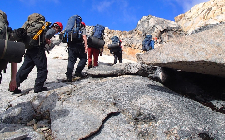 A group of people wearing backpacks hike up a rocky incline. 